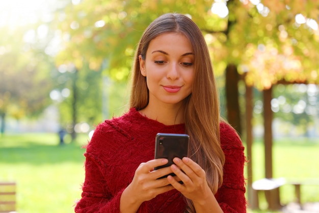 Gros plan d'une belle fille à l'aide de la navigation Internet sur un téléphone intelligent sur la saison d'automne ou d'hiver.