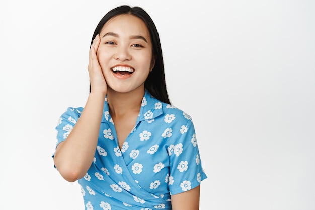 Gros plan d'une belle fille asiatique avec une peau du visage lisse et saine souriant et riant à la caméra debout en robe sur fond blanc