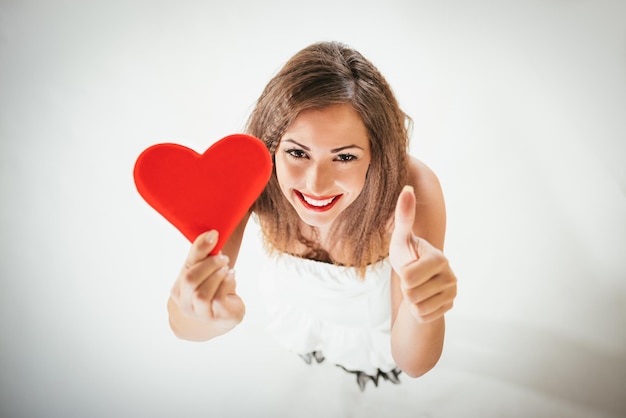 Photo gros plan d'une belle fille souriante tenant un coeur rouge avec le ventre vers le haut. mise au point sélective.