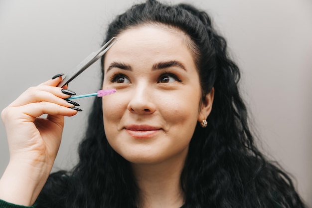 Gros plan d'une belle fille tenant une pince à sourcils dans sa main près de son visage dans le studio