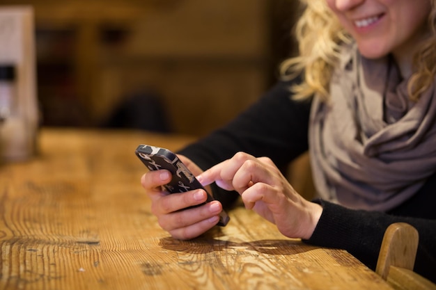 Gros plan d'une belle jeune femme assise confortablement à une table en bois et utilisant un smartphone à écran tactile