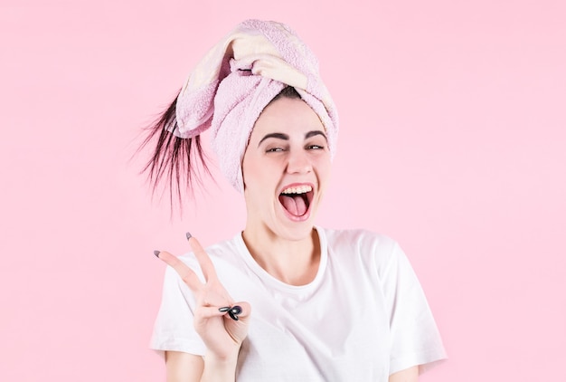 Gros plan de la belle jeune femme souriante avec une serviette de bain sur la tête, sur fond rose
