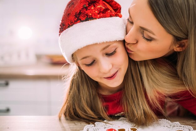 Gros plan belle jeune mère embrasse sa fille adolescente sur la joue dans la cuisine