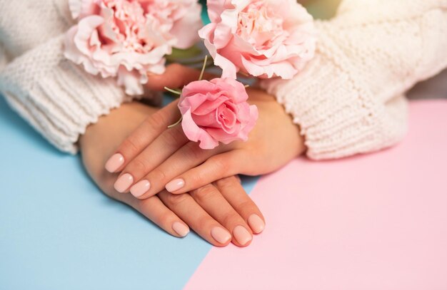 Gros plan de belles mains et fleurs sur fond rose et bleu multicolore