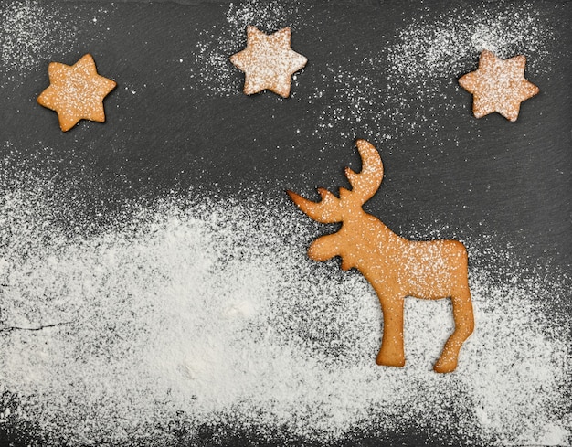 Photo gros plan sur des biscuits au pain d'épice avec des rennes de noël sur fond d'ardoise noire avec glaçage au sucre blanc en poudre et espace de copie, vue de dessus surélevée, directement au-dessus