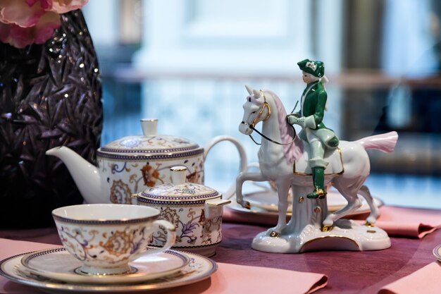 Gros plan blanc élégant service à thé de théière, sucrier et paire de thé, décoré de fleurs sur la table et figurine d'un cavalier