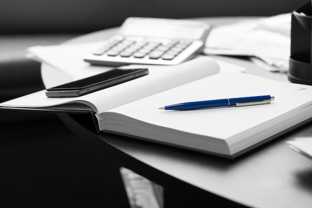 Gros Plan Sur Un Bloc-notes Blanc Avec Un Stylo Bleu Et Un Téléphone Portable Sur Une Table Ronde Noire.