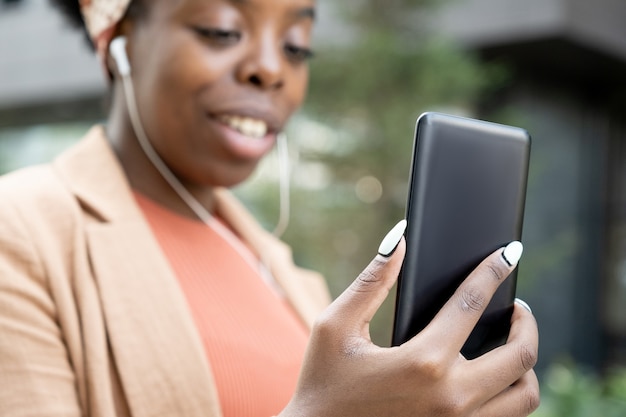 Gros plan sur une blogueuse africaine regardant l'écran de son téléphone portable tout en l'utilisant à l'extérieur