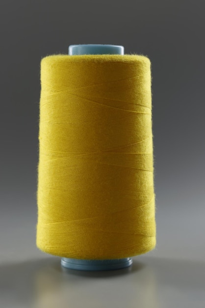 Gros plan sur une bobine de fil de couleur jaune sur fond gris, fil pour la couture. Fil brillant de haute qualité pour la couture. Passe-temps, couture, concept d'atelier