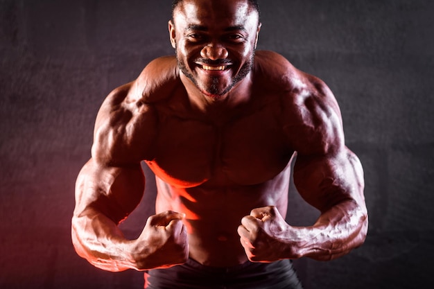 Gros plan d'un bodybuilder athlète masculin afro-américain posant démontrant le développement musculaire des bras biceps