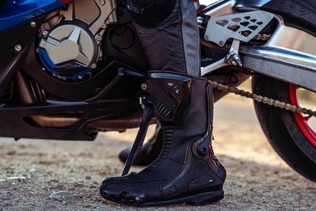 Un gros plan sur la botte d'un homme devant une moto