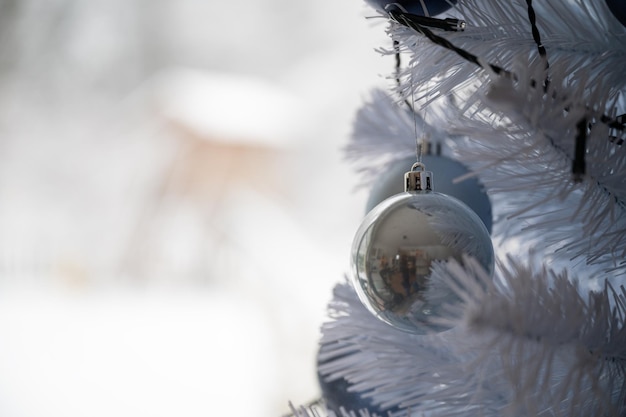 Gros plan d'une boule de Noël en verre bleu accrochée à un arbre de Noël blanc avec une nature enneigée en arrière-plan.