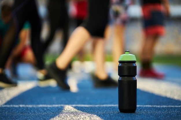 Gros plan sur une bouteille de sport noire avec un capuchon vert se dresse sur un tapis roulant en caoutchouc bleu avec une ligne blanche