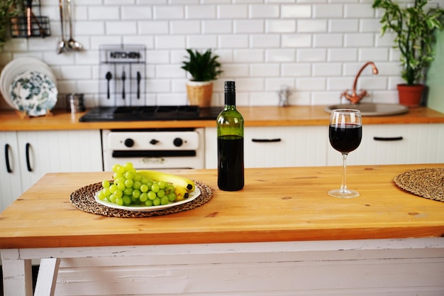 Gros plan d'une bouteille et d'un verre de vin rouge avec des baies et des fruits sur la plaque Préparation sur table pour les rencontres en cuisine