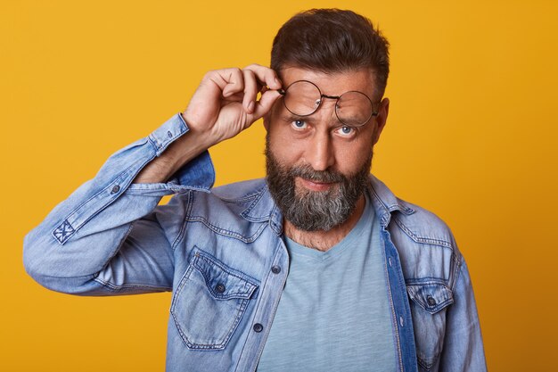 Gros plan de branché à la mode guy hipster d'âge moyen avec moustache garnie et barbe posant isolé sur mur de studio