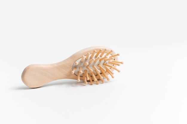 Gros plan d'une brosse à cheveux en bois sur une surface blanche.