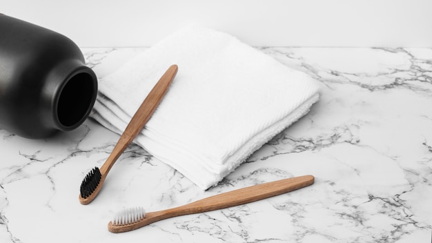 Gros plan de la brosse à dents en bois; serviettes blanches et pot sur une table en marbre