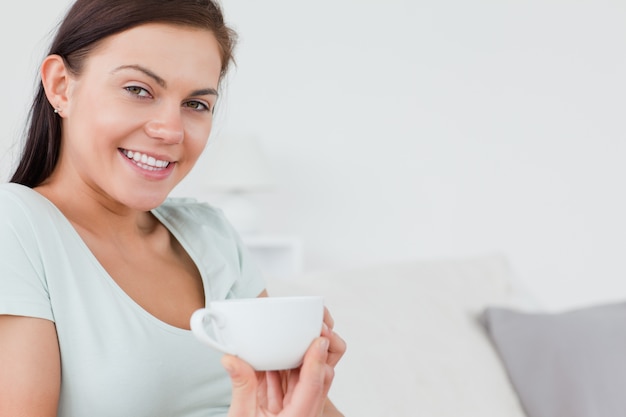 Gros plan d&#39;une brune assise sur un canapé avec une tasse de café