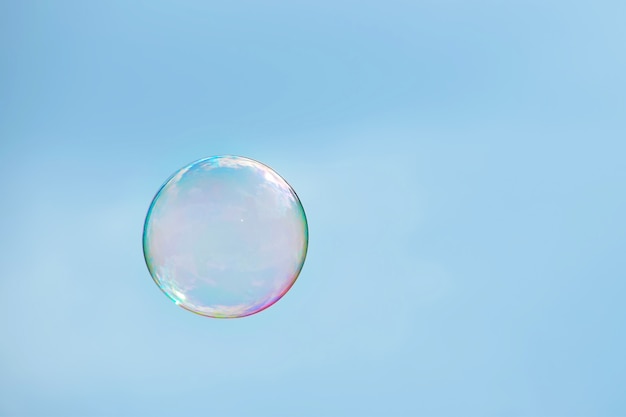 Gros plan sur une bulle de savon multicolore sur un ciel bleu clair