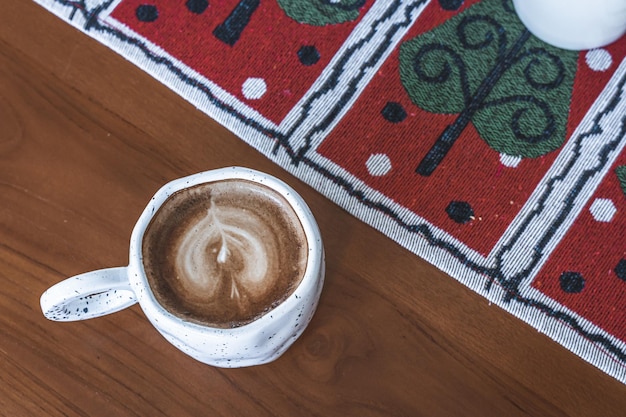 Gros plan sur un café au lait chaud avec de la mousse de lait latte art dans une tasse avec des décors de Noël et des boules d'arbre de Noël sur un bureau en bois Célébrant Joyeux Noël et Nouvel an