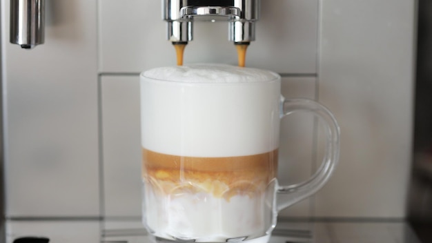 Gros plan de café versé dans une tasse en verre avec du lait faisant du cappuccino à l'aide de la machine à café automatique Boisson pour le petit déjeuner