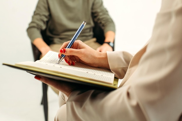 Gros plan d'un cahier avec un stylo dans les mains d'un psychologue prenant des notes lors d'une séance de psychothérapie avec un homme Psychothérapie psychothérapie