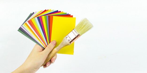 Gros plan sur un catalogue de peintures avec une brosse à bois dans la main d'une femme, diverses palettes de couleurs, des échantillons pour la définition des couleurs.