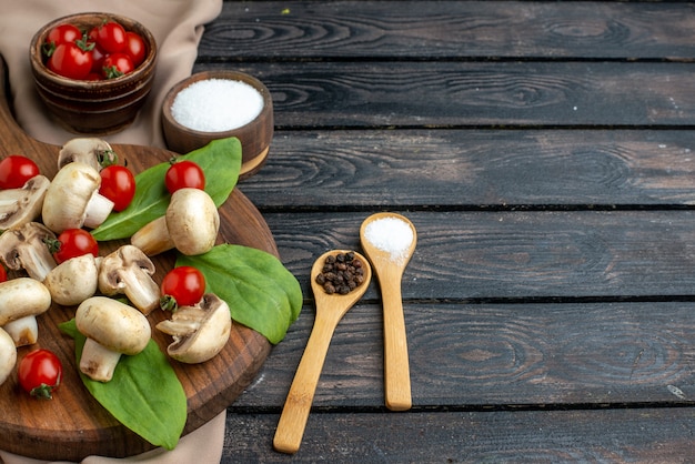 Gros plan sur des champignons frais crus et des épices de tomates sur une serviette en bois sur fond noir