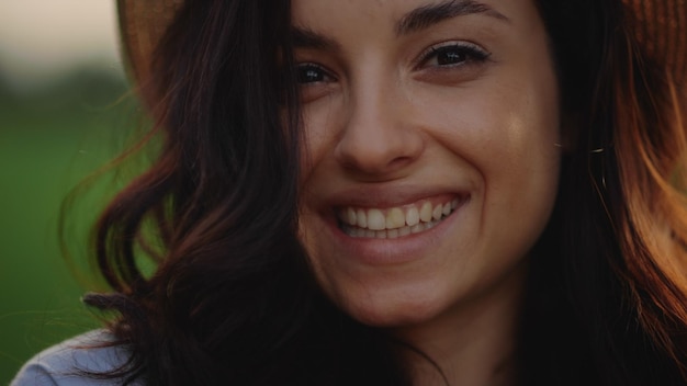 Gros plan charmant visage de jeune fille regardant la caméra à l'extérieur Portrait de visage de femme heureuse souriant sur le terrain au coucher du soleil