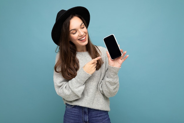 Gros plan de la charmante jeune femme heureuse portant un chapeau noir et un pull gris