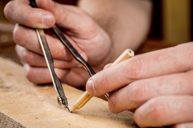 Un gros plan d'un charpentier mâle marque avec un compas métallique et un crayon sur une barre en bois