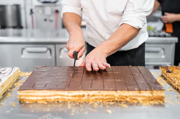 Gros plan d'un chef pâtissier couper un gros gâteau en portions