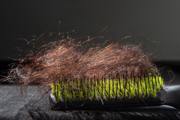 Gros plan d'un chignon de cheveux humains bruns incurvés tombant d'une femme allongée sur un peigne noir et vert.