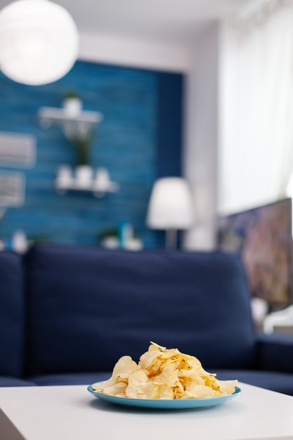 Gros plan de chips snack assis sur une table basse. Salon moderne sans personne avec des meubles et des murs bleus, joliment décoré. Décoration assez simple de l'appartement. Décoration rétro élégante, cosy.