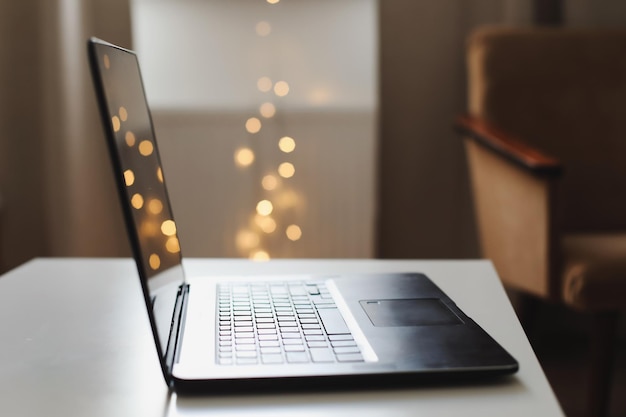 Gros plan sur un clavier d'ordinateur portable avec un écran vierge sur une table par un arrière-plan flou de lumières bokeh dans la maison ou le bureau lumière du soleil moderne le matin