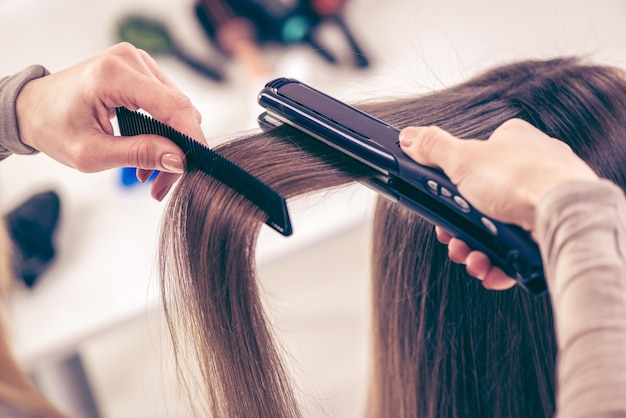 Gros plan d'un coiffeur lissant de longs cheveux bruns avec des fers à cheveux.