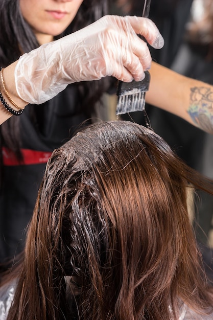 Gros plan sur une coiffeuse brune qui teint en profondeur les cheveux d'une cliente alors qu'elle est assise sur une chaise dans un salon de beauté