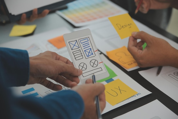 Gros plan sur la conception filaire de l'interface d'application mobile avec le développeur ux et le concepteur d'interface utilisateur sur la table avec le résumé du client et le code couleur dans un bureau moderne. Agence de développement numérique créatif