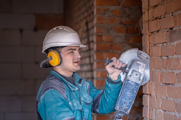 Gros plan d'un constructeur dans un casque de protection dans un lieu de travail fonctionne avec un outil de coupe.