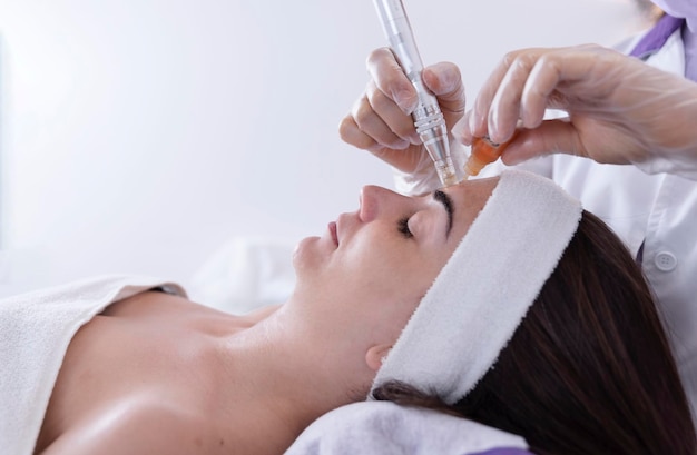 Gros plan sur Cosmetologistbeautician appliquant un traitement dermapen facial sur le visage d'une jeune femme cliente dans un salon de beautéCosmétologie et soins de la peau professionnels rajeunissement du visage