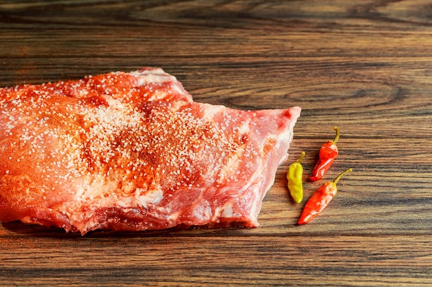 Gros plan d'une côte de porc frite juteuse appétissante sur une planche à découper en bois avec de la poudre épicée, un pinceau et de l'oli...