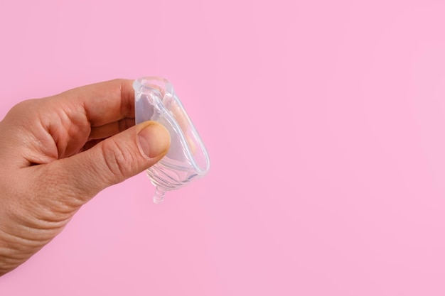 Gros plan sur une coupe menstruelle en silicone pliable à la main pour femme sur fond rose
