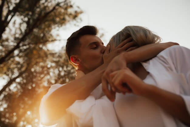 Gros plan d'un couple amoureux s'embrasse. L'homme touche le visage de la petite amie avec tendresse en soirée d'été.