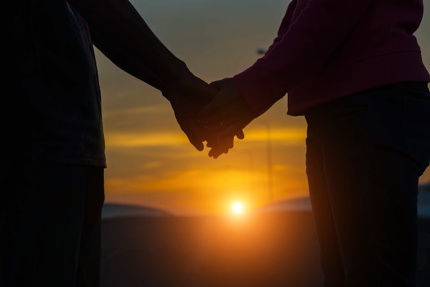 Gros plan d'un couple d'amoureux se tenant la main en marchant au coucher du soleil