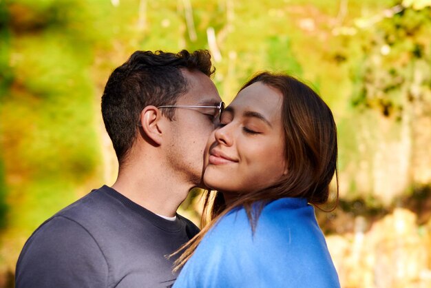 Un gros plan d'un couple debout au soleil dans un parc et s'embrasser sur la joue