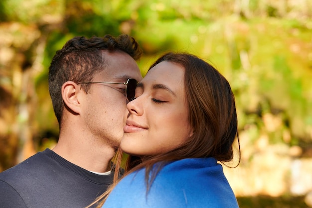 Un gros plan d'un couple debout au soleil dans un parc et s'embrasser sur la joue