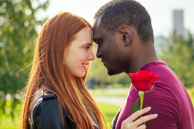 Photo gros plan d'un couple interracial tenant une rose blanche dans le parc d'automne du printemps
