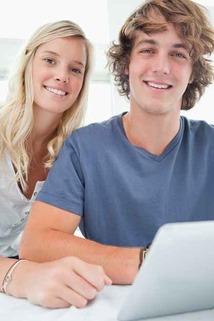 Gros plan couple souriant tenant une tablette et en regardant la caméra