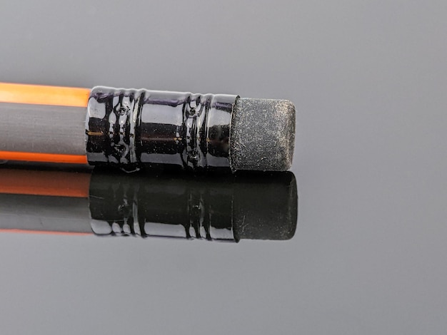 Gros plan d'un crayon gomme en caoutchouc noir avec réflexion sur un panneau acrylique noir
