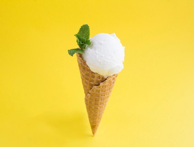 Gros plan sur la crème glacée à la vanille dans un cône de gaufre sur le fond jaune